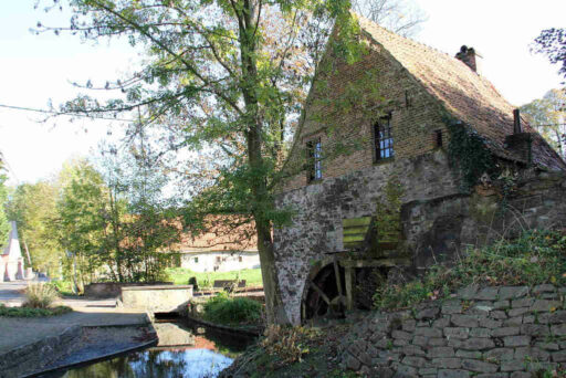 Maison en brique avec une roue à eau sur le côté, située à côté d’un canal et entourée d’arbres